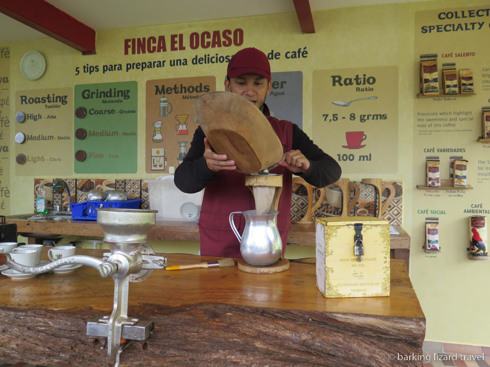 A photo of a man pouring ground coffee grinds into a filter on top of a metal jug